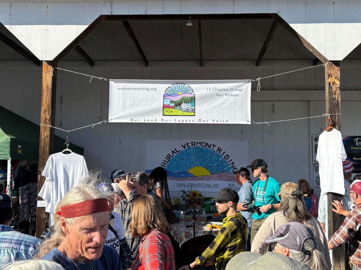 People gathered at an outdoor stage under a fair banner